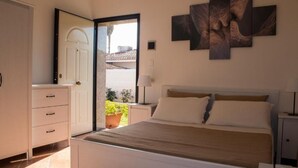 Une chambre à coucher comprenant un lit, une commode, une table de chevet, une lampe et une œuvre d’art accrochée au mur.