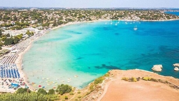 Vue aérienne d’une zone côtière avec une plage, des bateaux et une mer bleue et limpide.