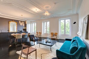 Een moderne woonkamer met een eethoek, grote ramen en een turquoise bank.