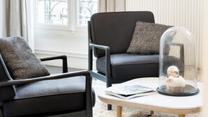 Een moderne woonkamer met twee zwarte leren banken, een witte vloerkleed en een glazen koepel over een decoratief object.