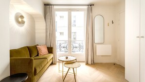 Een moderne woonkamer met een bank, een klein rond tafeltje en een groot raam met gordijnen.