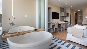 A modern bathroom with a large bathtub, a wooden tray, and a glass of water.