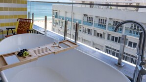 A modern bathroom with a large bathtub, a glass shower enclosure, and a view of the ocean and buildings.