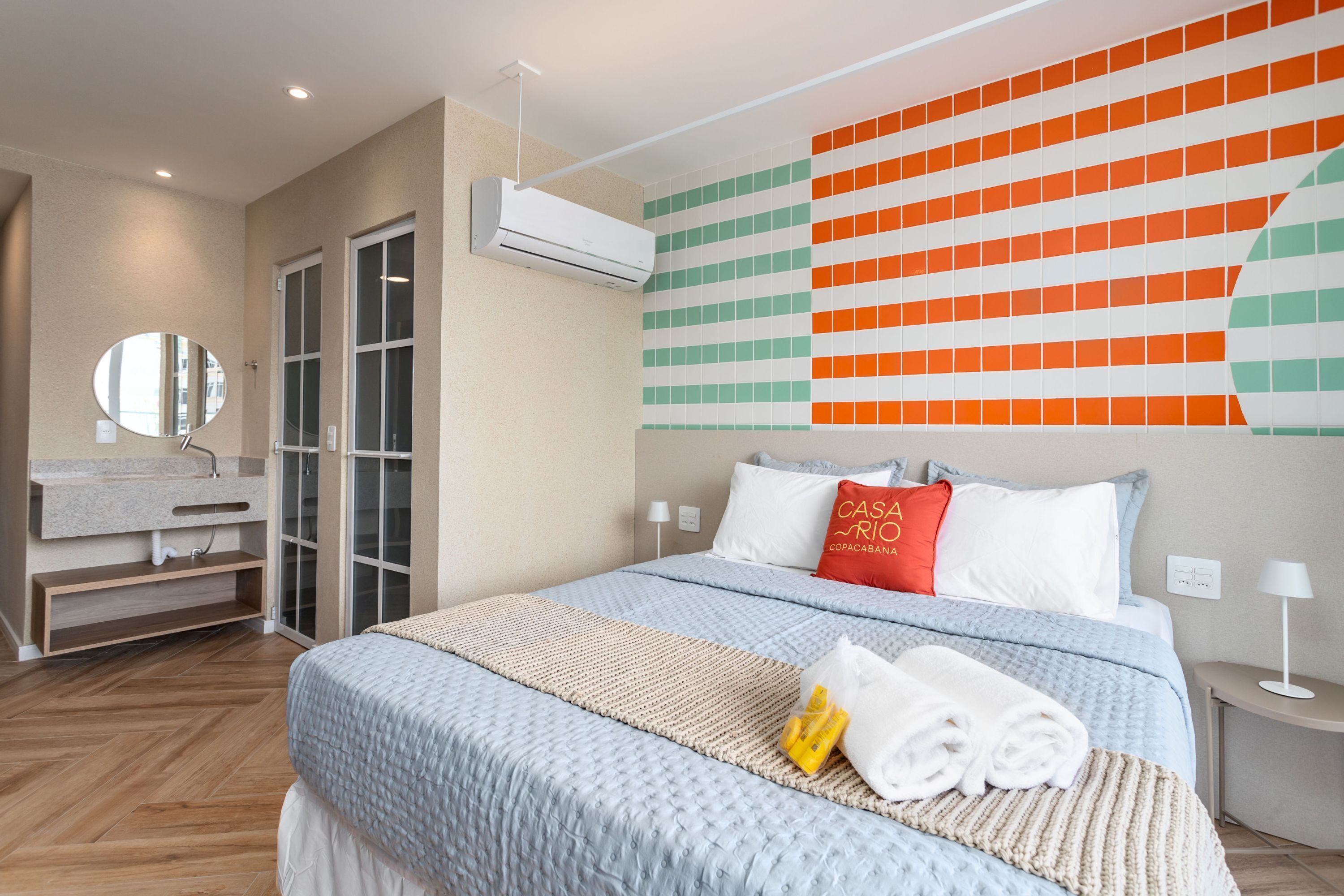A modern hotel room with a large bed, a bathroom with a mirror, and a wall with a colorful pattern.