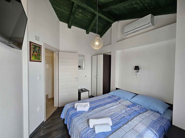 A bedroom with a bed, a bedside table, a mirror, a wardrobe, and a hanging light fixture.