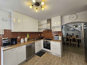 A modern kitchen with white cabinets, a stove, a microwave, and a dining area with a table and chairs.