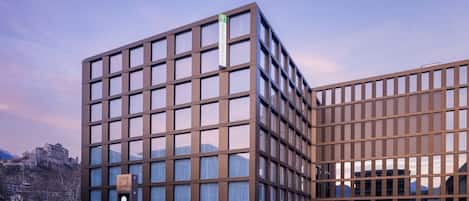 Un hôtel moderne avec une façade composée d’une série de fenêtres et une enseigne indiquant la présence d’une cour intérieure.