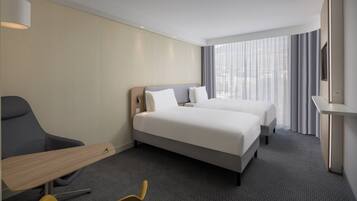 A hotel room with two beds, a desk, a chair, and a large window with curtains.