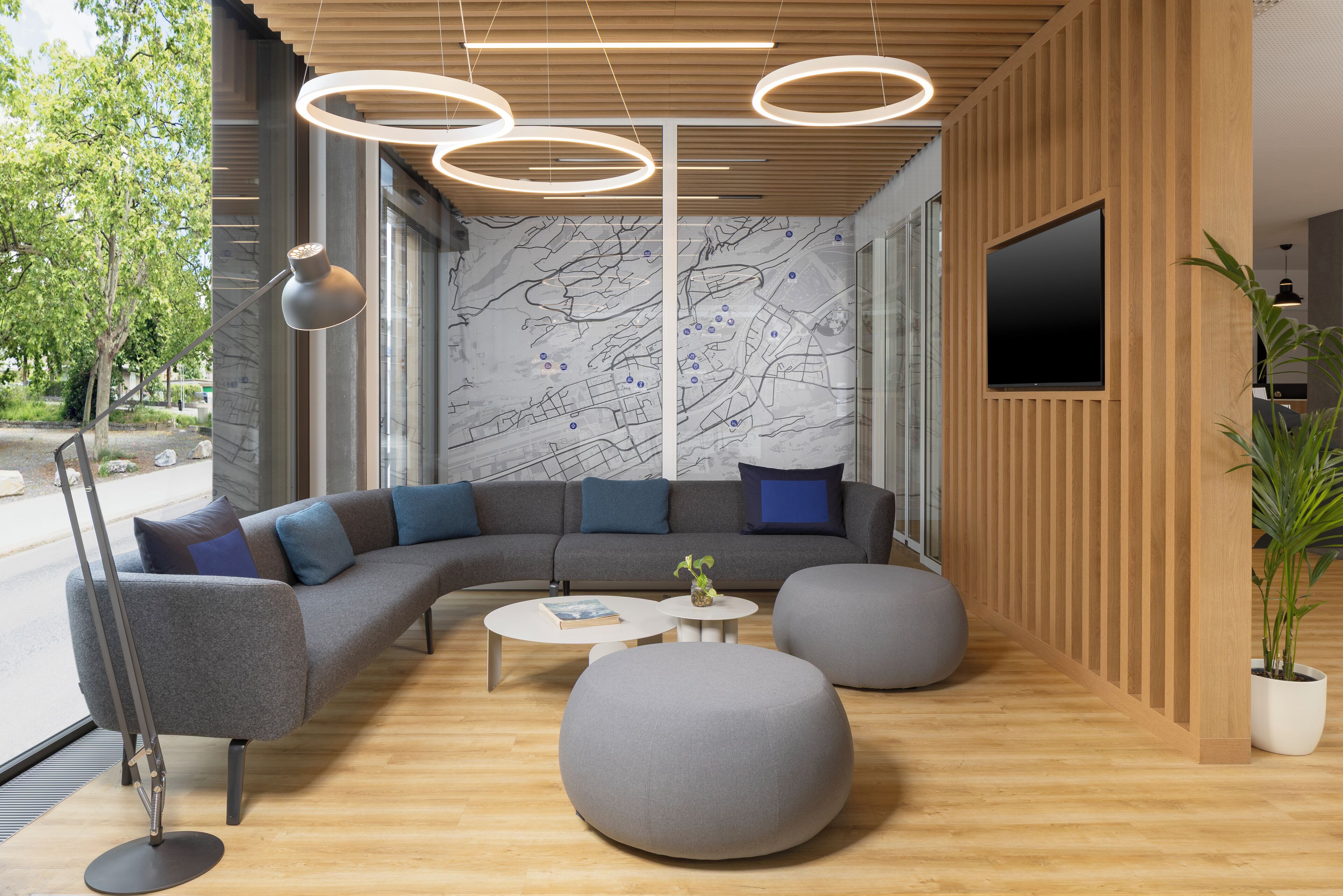Un interior moderno con un sofá modular, otomanos redondos, una mesa de centro y un televisor montado en una pared de madera.