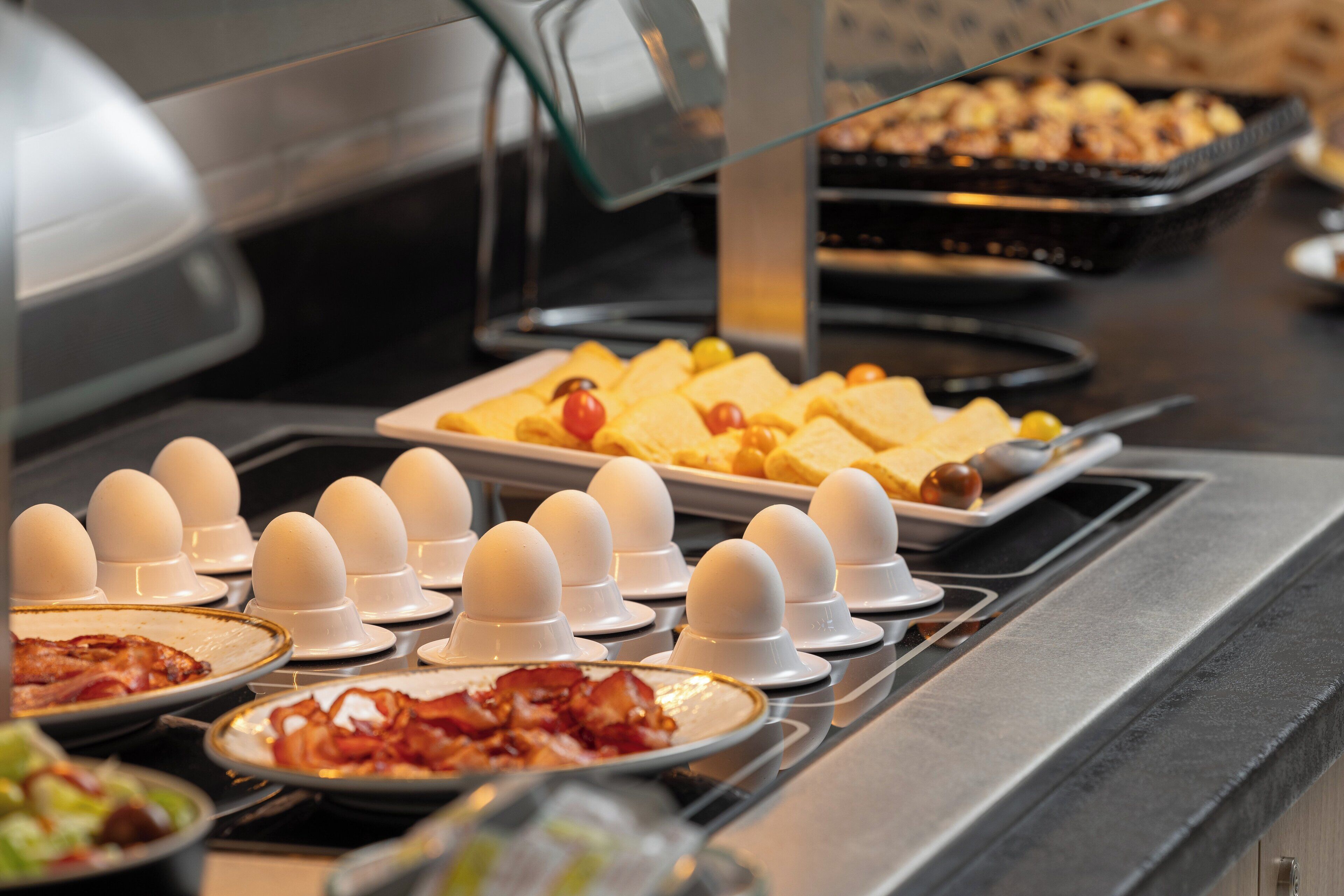 En buffet med forskellige spiser, herunder æg, bacon og bagværk.