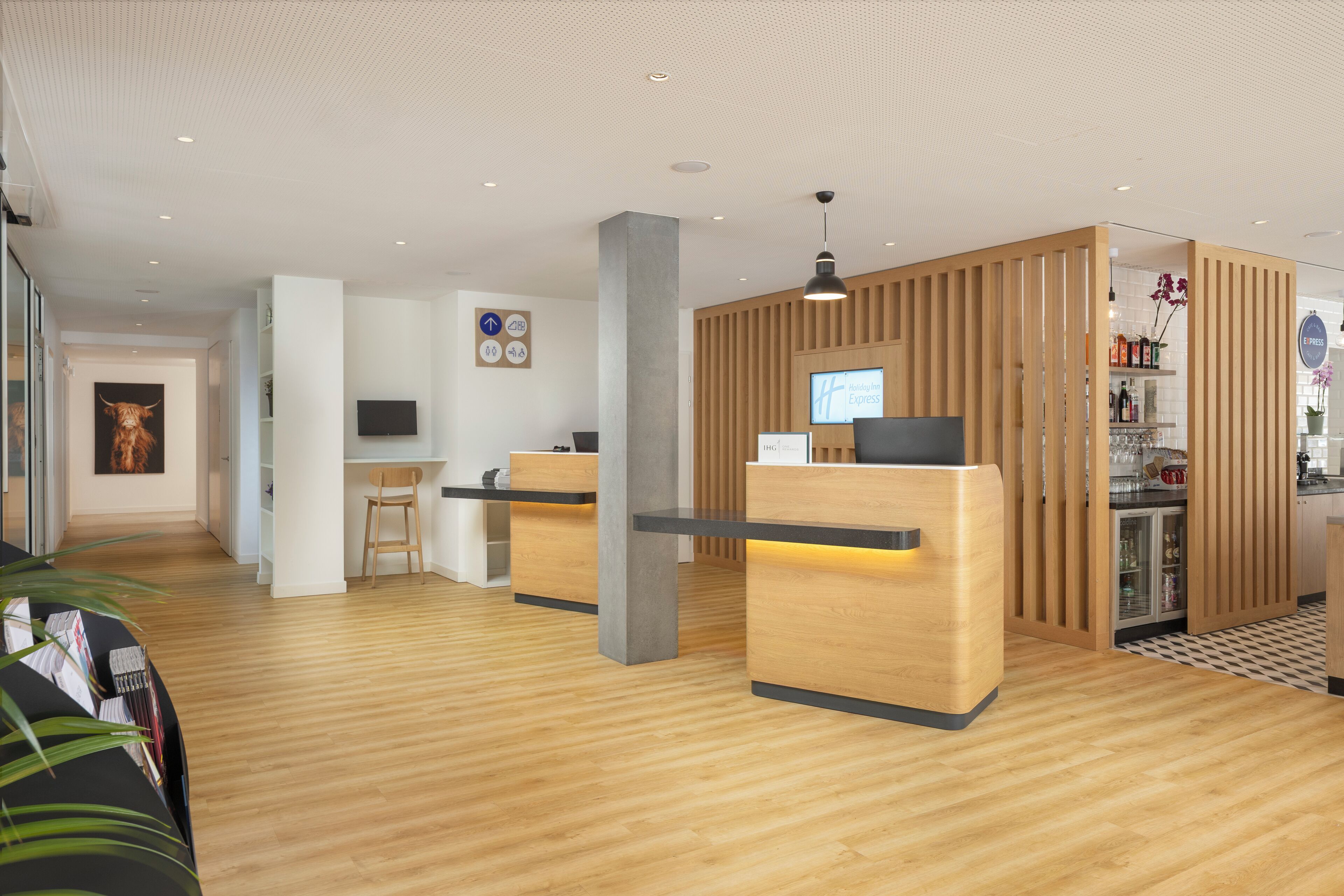 A modern reception area with wooden reception desks, a flat-screen TV, and a coffee bar with a refrigerator.
