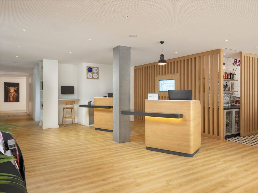 A modern reception area with wooden reception desks, a flat-screen TV, and a coffee bar with a refrigerator.