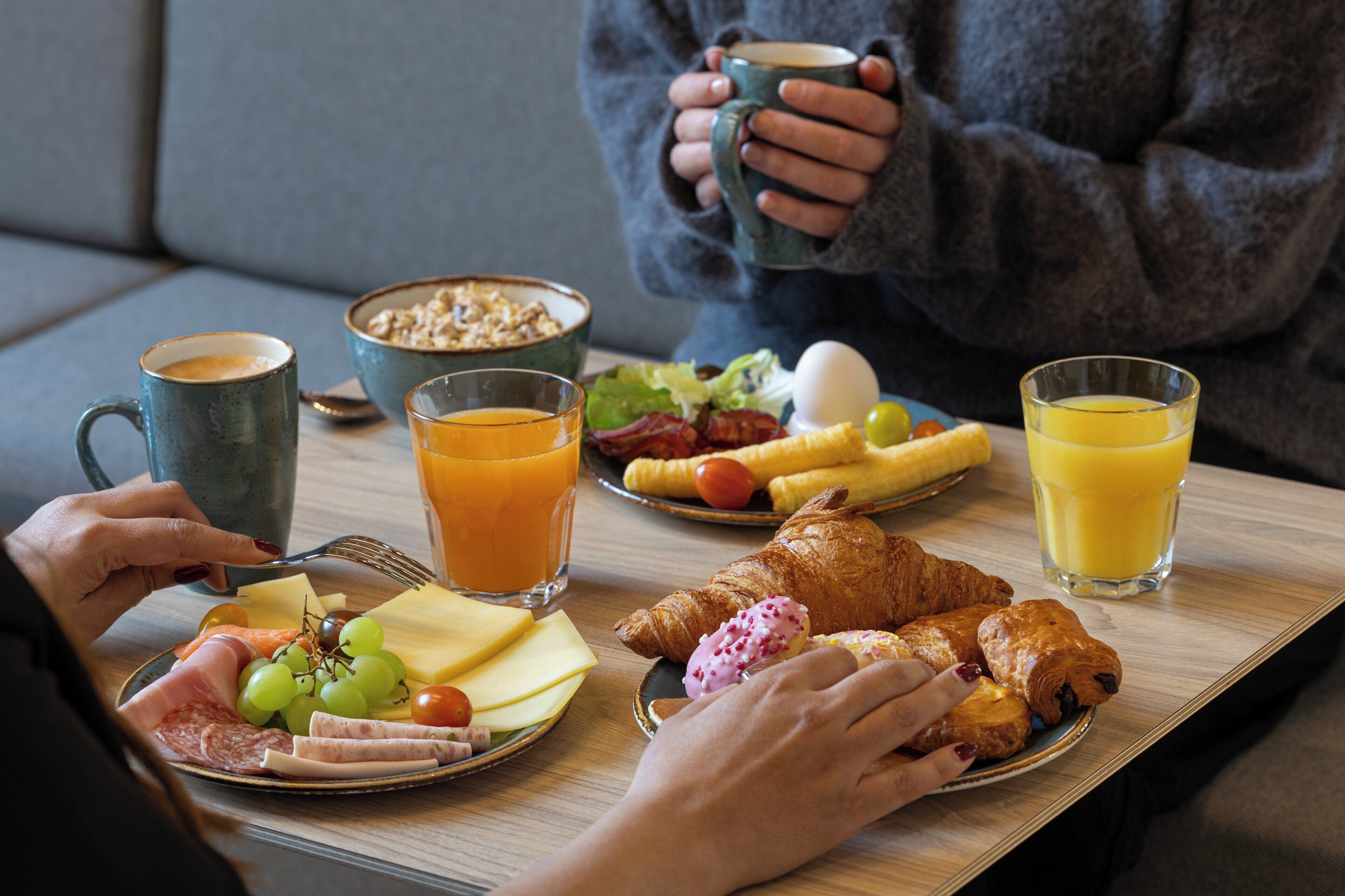 Ett frukostbricka med croissanter, ost, skinka och frukt på ett träbord.