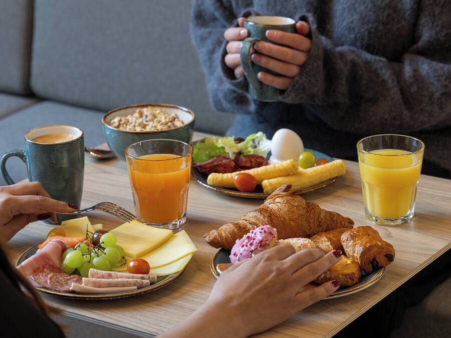 Bandeja de desayuno con cruasanes, queso, jamón y frutas sobre una mesa de madera.