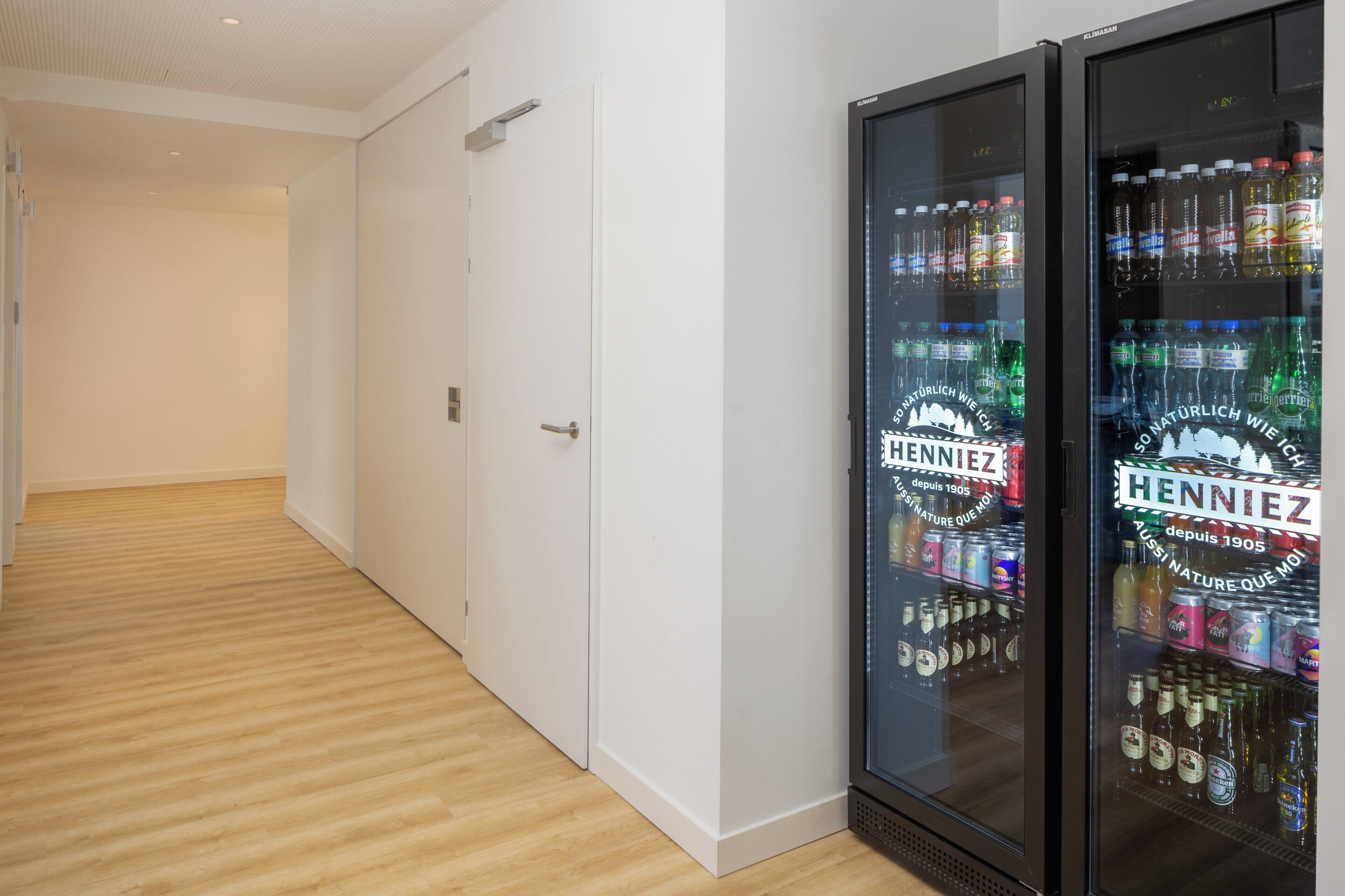 A hallway with a refrigerator stocked with beverages and a door at the end.