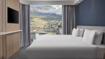 Un hotel moderno con una cama grande, un televisor de pantalla plana montado en la pared y vistas a un paisaje montañoso.