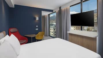 A hotel room with a large bed, a TV mounted on the wall, a small table, and two chairs.