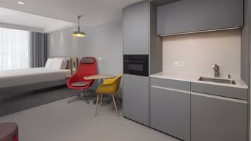 Habitación de hotel moderna con cama, kitchenette, una silla roja y amarilla, y un ventanal grande.