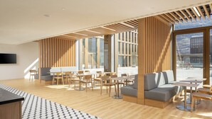 Ein modernes Interieur mit Holzböden, unterschiedlichen Sitzmöglichkeiten und großen Fenstern mit Blick ins Freie.