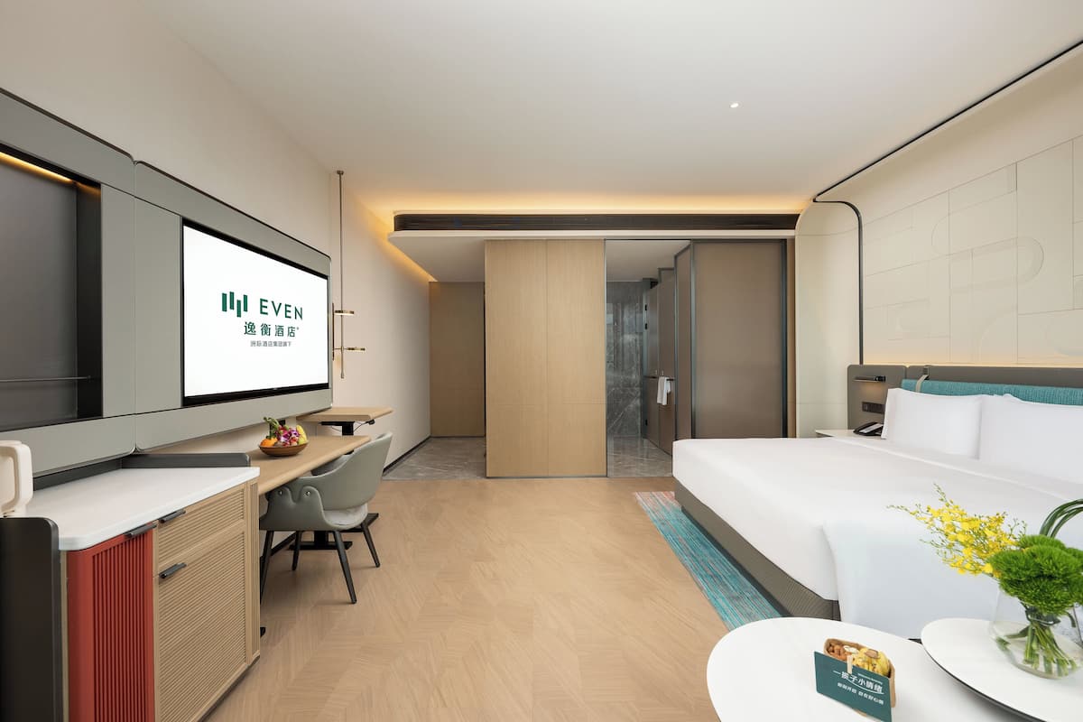 Una habitación de hotel moderna con una cama, un escritorio, un televisor y una pequeña mesa con un jarrón de flores.