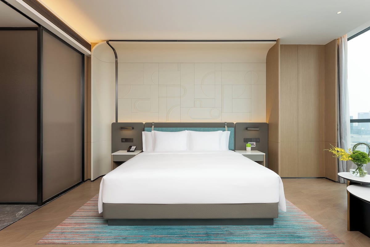 Una habitación de hotel moderna con una cama grande, una mesita de noche, un escritorio y vistas a la ciudad.