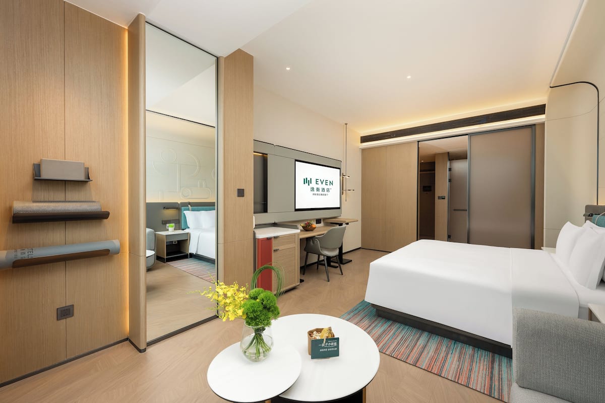 Una habitación de hotel moderna con cama, escritorio, silla, televisión y una pequeña mesa con un florero.