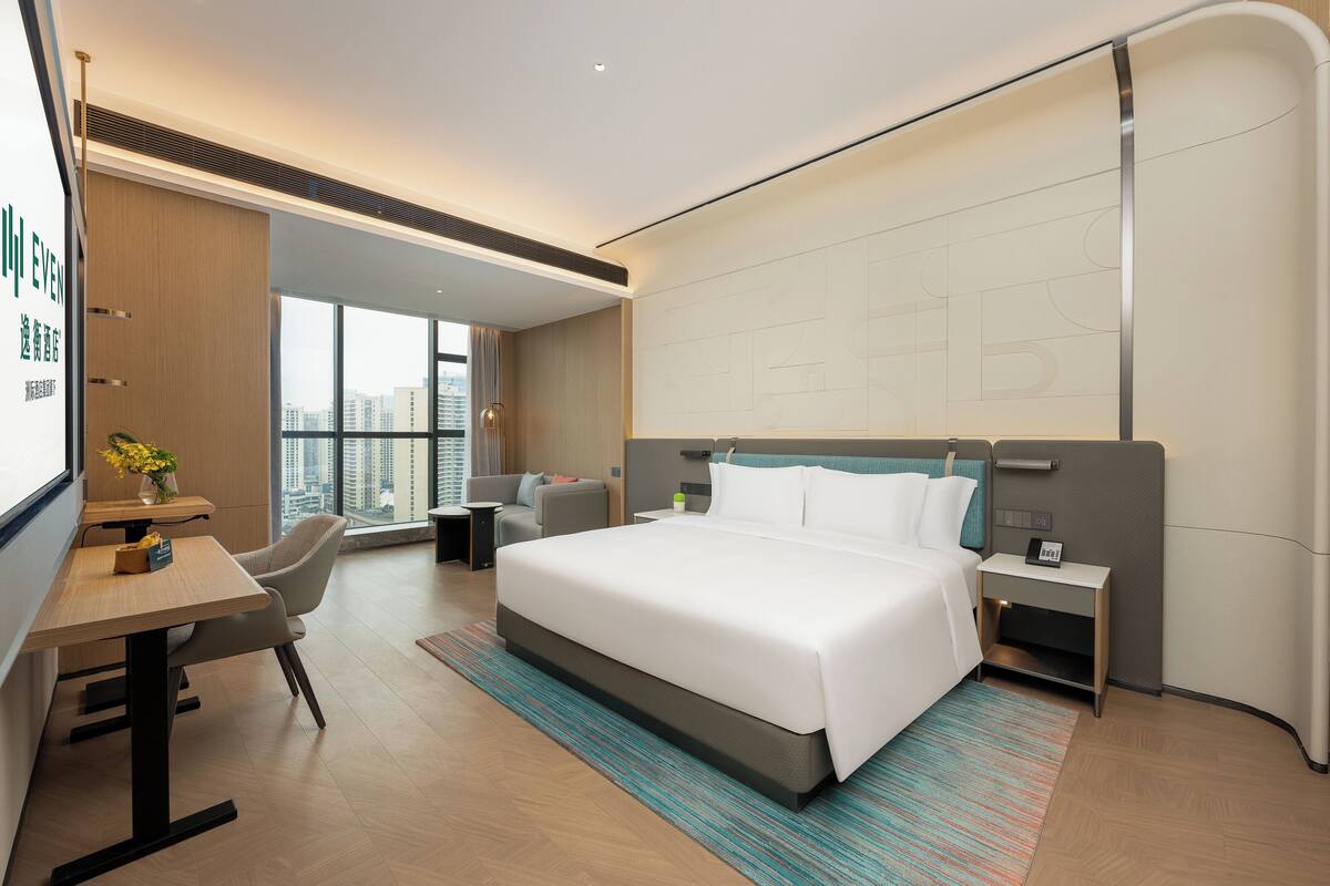 Habitación de hotel moderna con una cama grande, un escritorio, una silla y vistas a la ciudad.