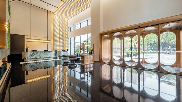 Un vestíbulo amplio con piso reflectante, una recepción y grandes ventanales que ofrecen vistas al exterior.