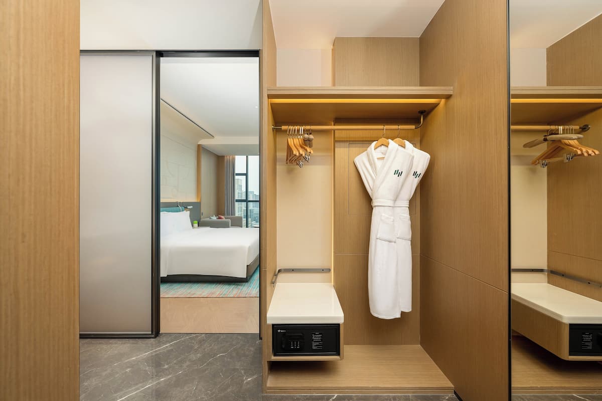 Habitación de hotel con cama, bata colgada en un perchero y una mesita con panel de control.