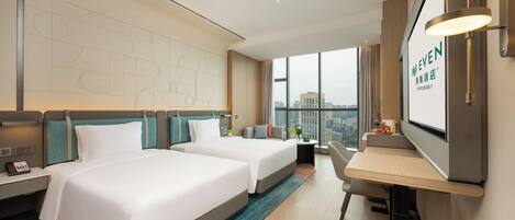A hotel room with two beds, a desk, a chair, a TV, and a large window with a city view.