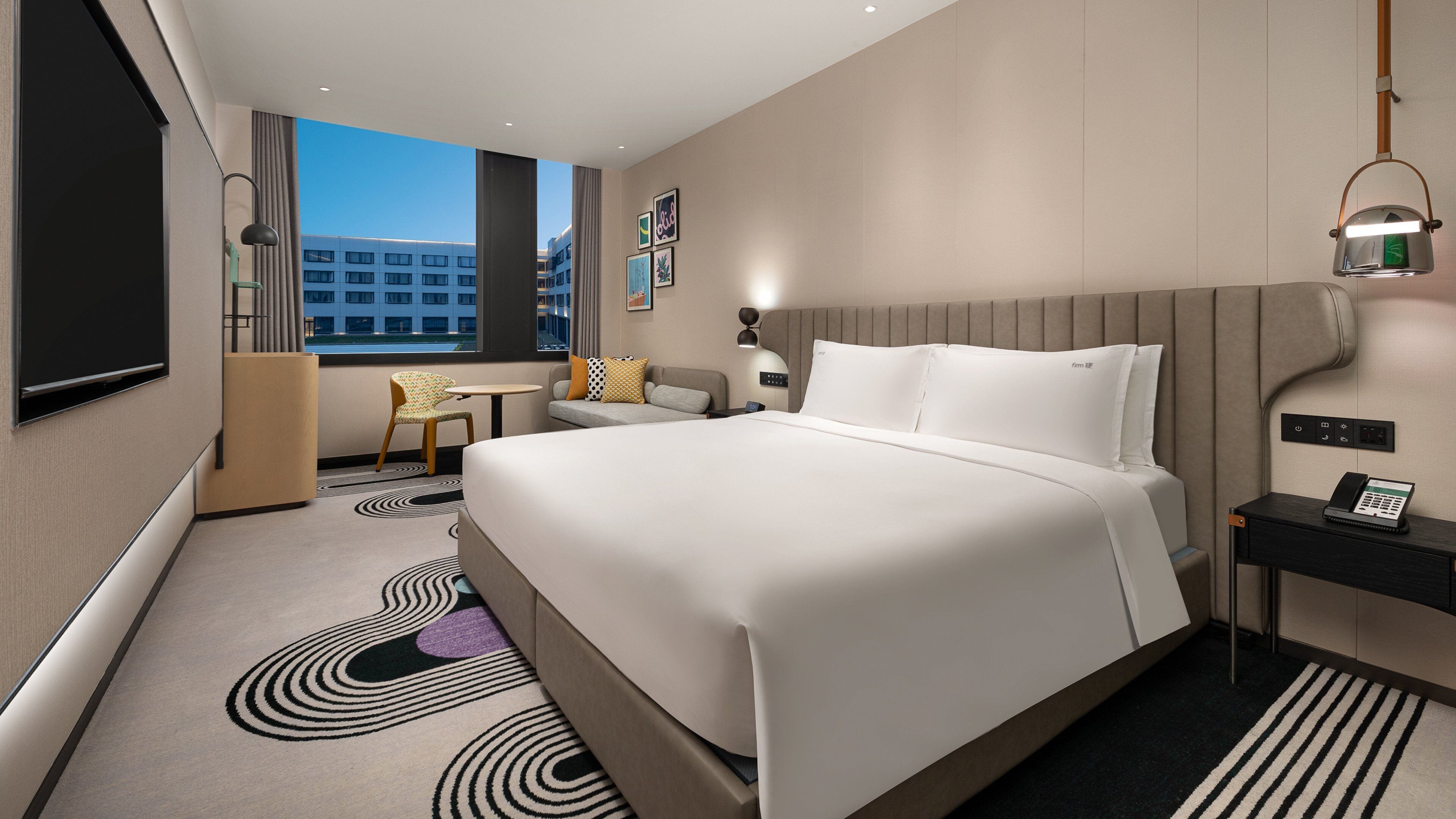 Habitación de hotel moderna con una cama grande, un escritorio, una silla y vista a la ciudad.