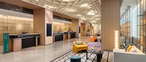 A modern lobby with a geometric ceiling, reception desks, seating areas, and a patterned floor.