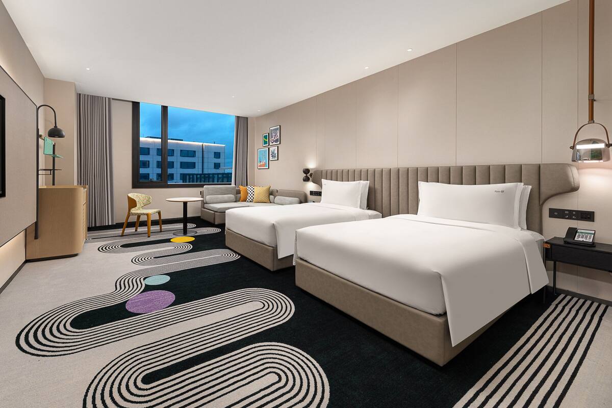 A modern hotel room with two beds, a TV, a desk, and a view of the city.