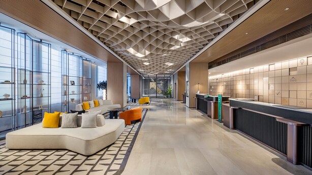 Un moderno vestíbulo de hotel con una larga recepción, área de estar con sofás y sillones, y piso con diseño.