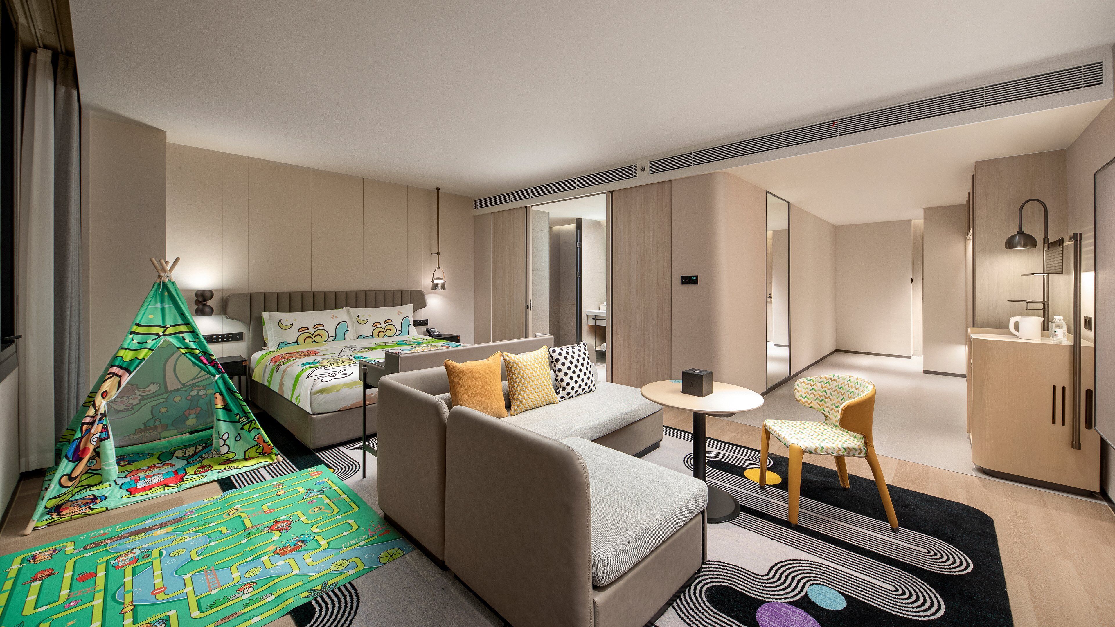 A modern hotel room with a bed, sofa, and a small table.