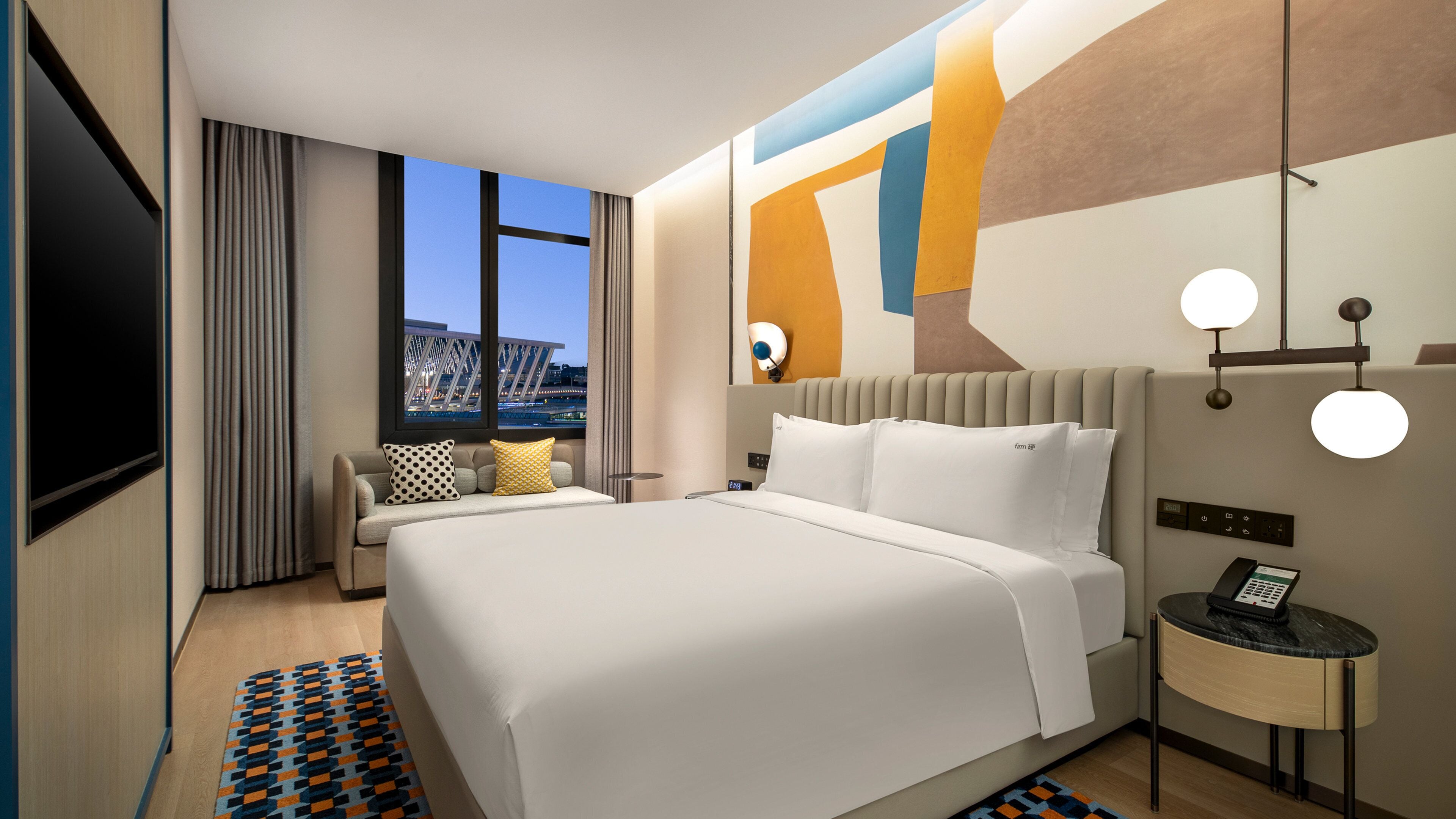 Una habitación de hotel moderna con una cama grande, un área de descanso, un televisor y vistas a la ciudad.