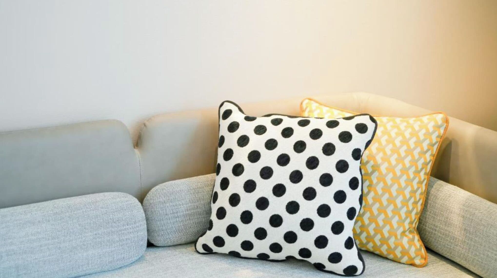 Un canapé avec trois coussins : un avec un motif à pois noirs et blancs, un avec un motif à chevrons jaunes et blancs, et un coussin uni de couleur grise.