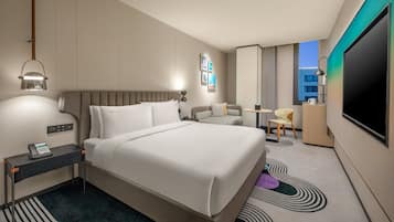 A hotel room with a bed, bedside table, lamp, chair, desk, and a flat-screen TV.