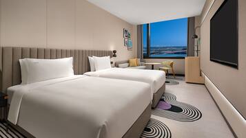 A hotel room with two beds, a sofa, a small table, a chair, and a large window with a city view.