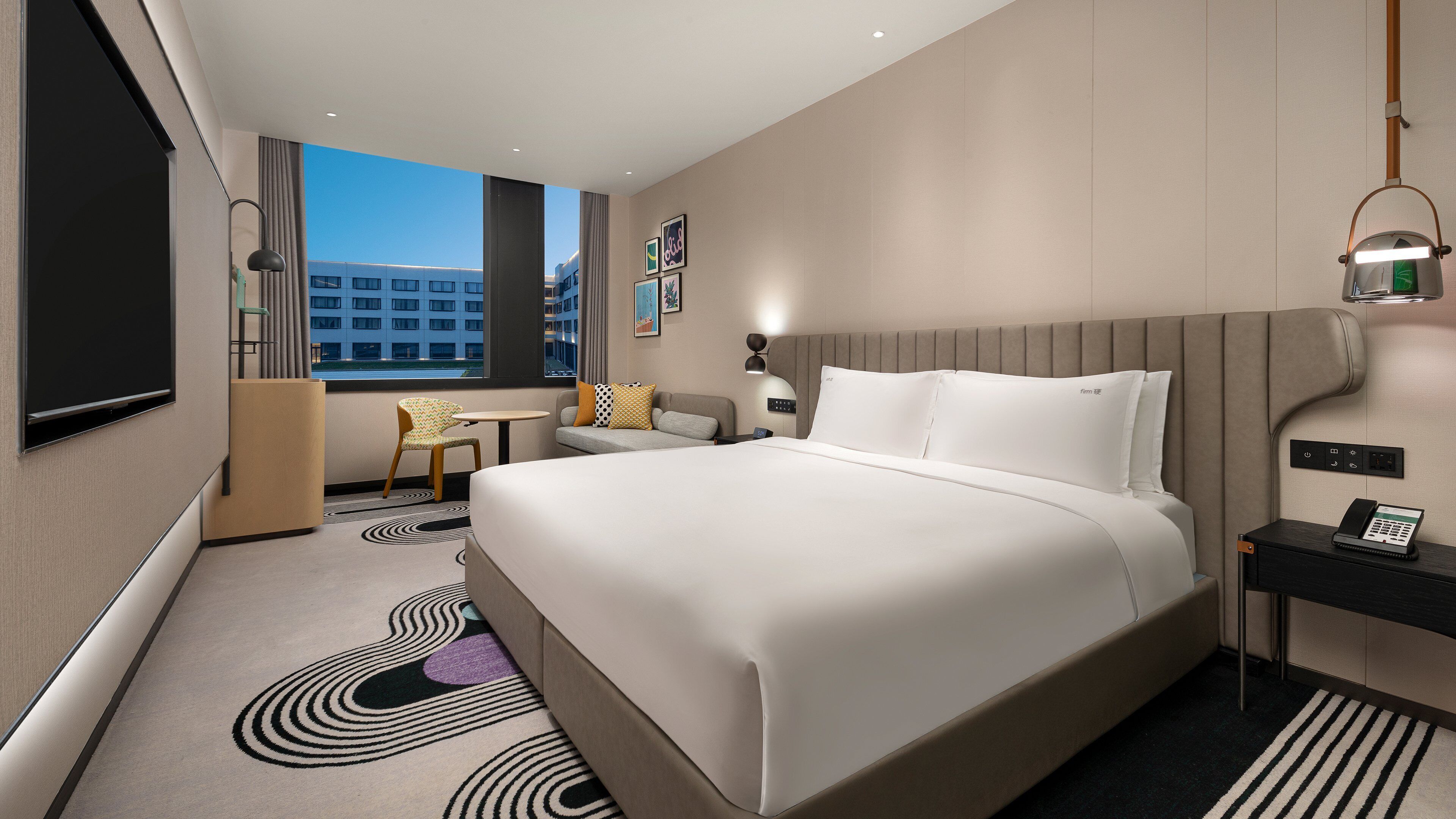 A modern hotel room with a large bed, a desk, a chair, and a view of the cityscape.
