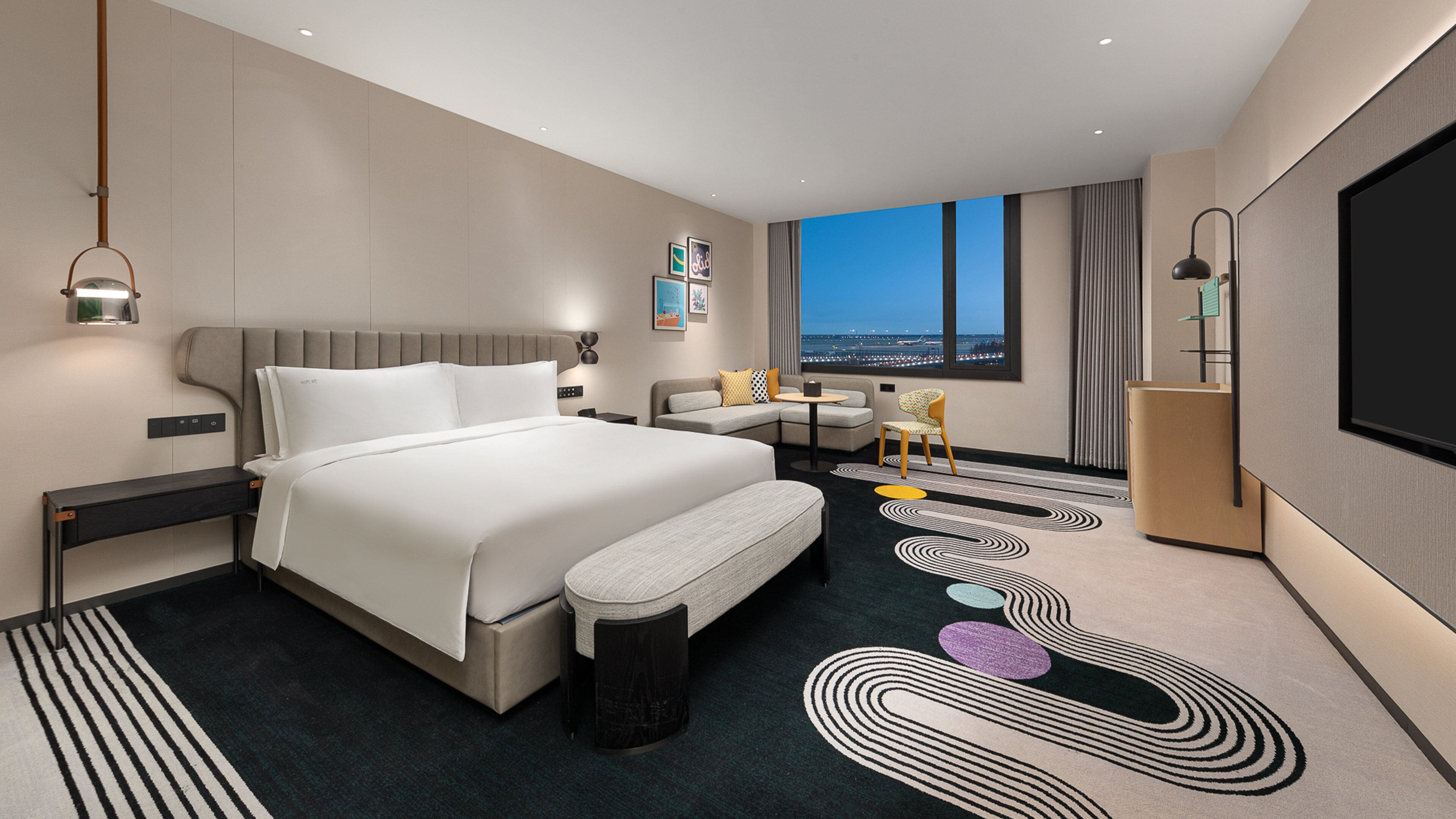 Habitación de hotel moderna con una cama grande, un sofá, un escritorio y vistas a la ciudad.