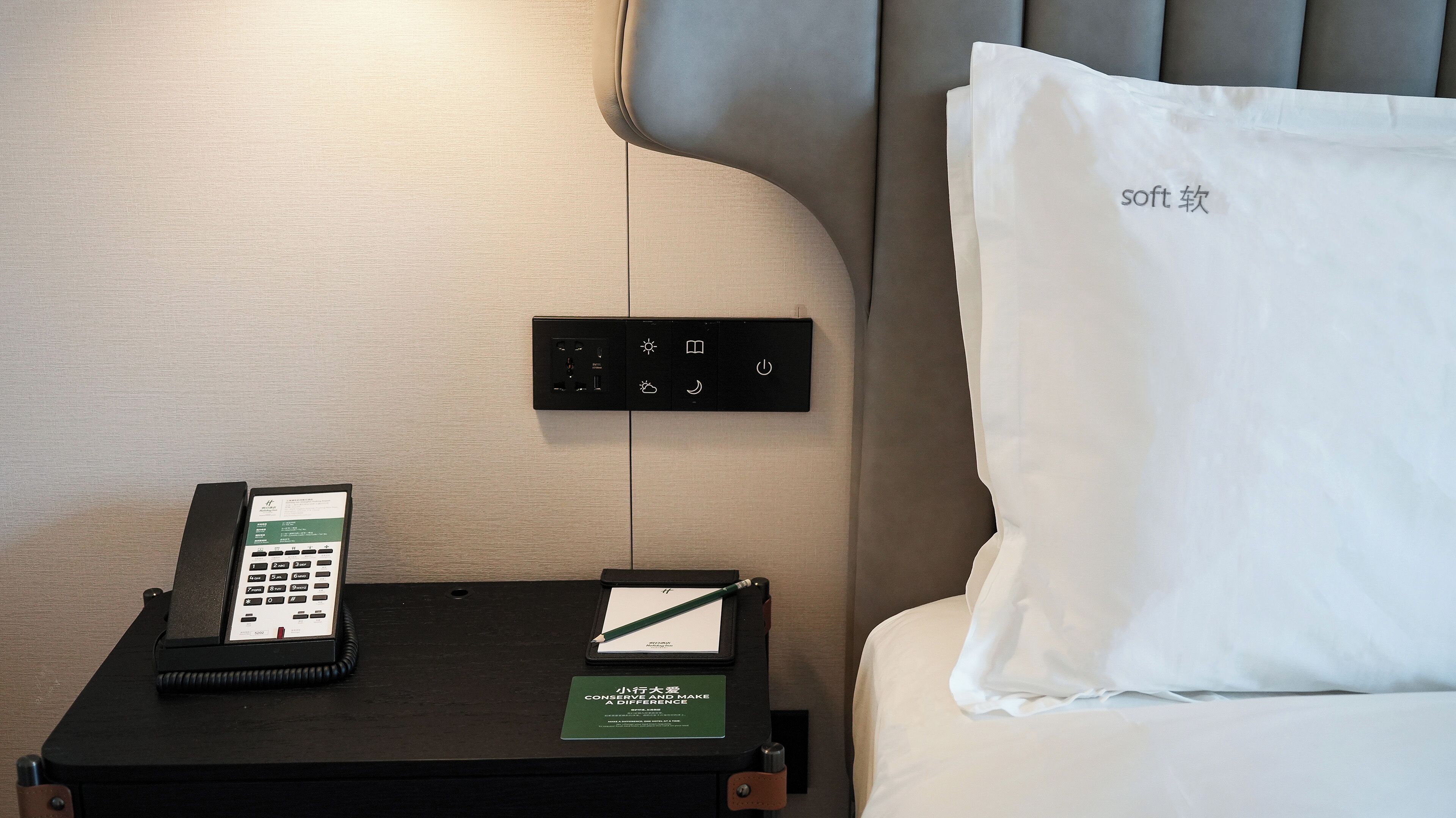 Habitación de hotel con una cama, una mesita de noche con un teléfono, una tarjeta pequeña y un panel de control en la pared.
