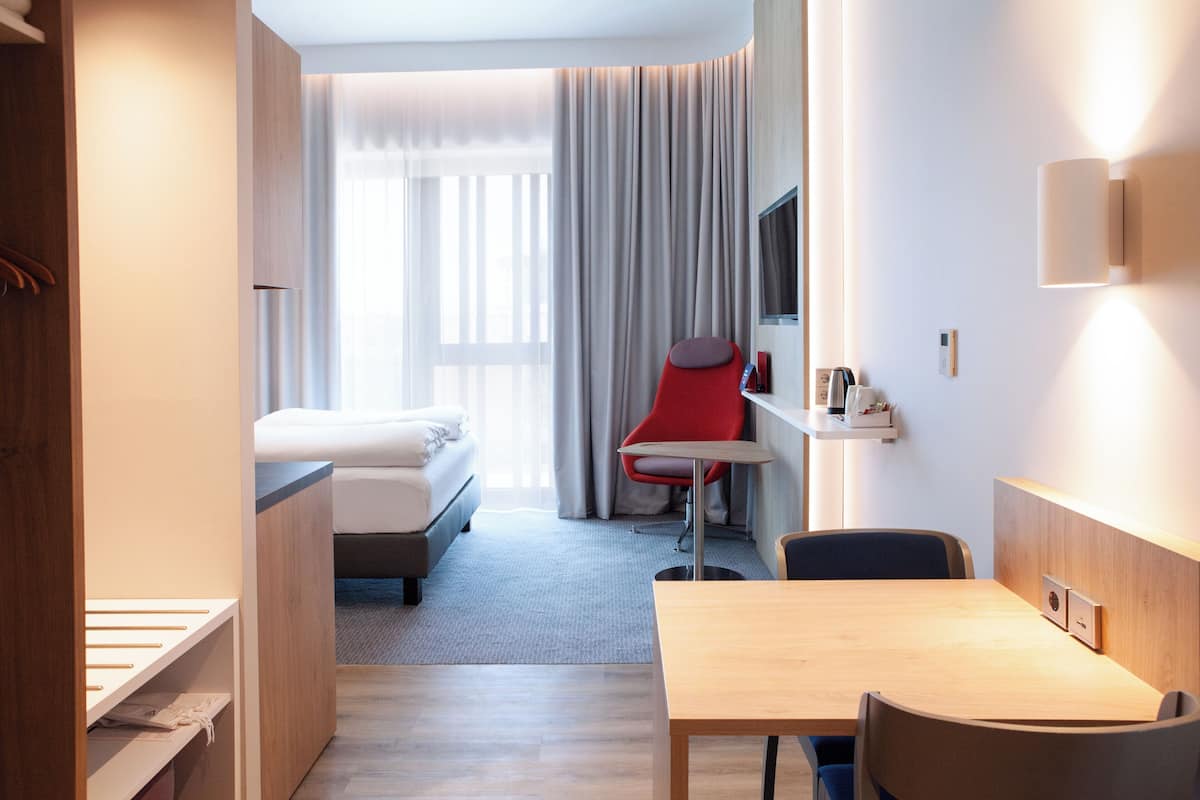 A hotel room with a bed, a desk, a chair, a TV, and a window with curtains.