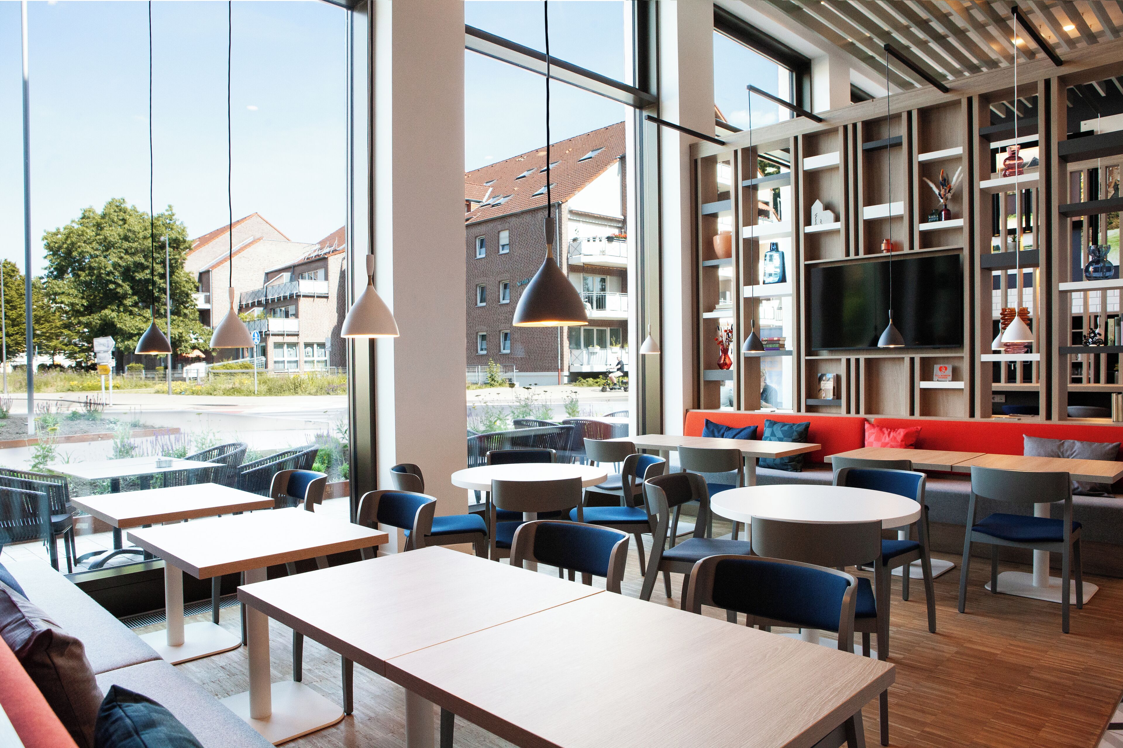 A modern cafe with large windows, seating areas, and a TV.