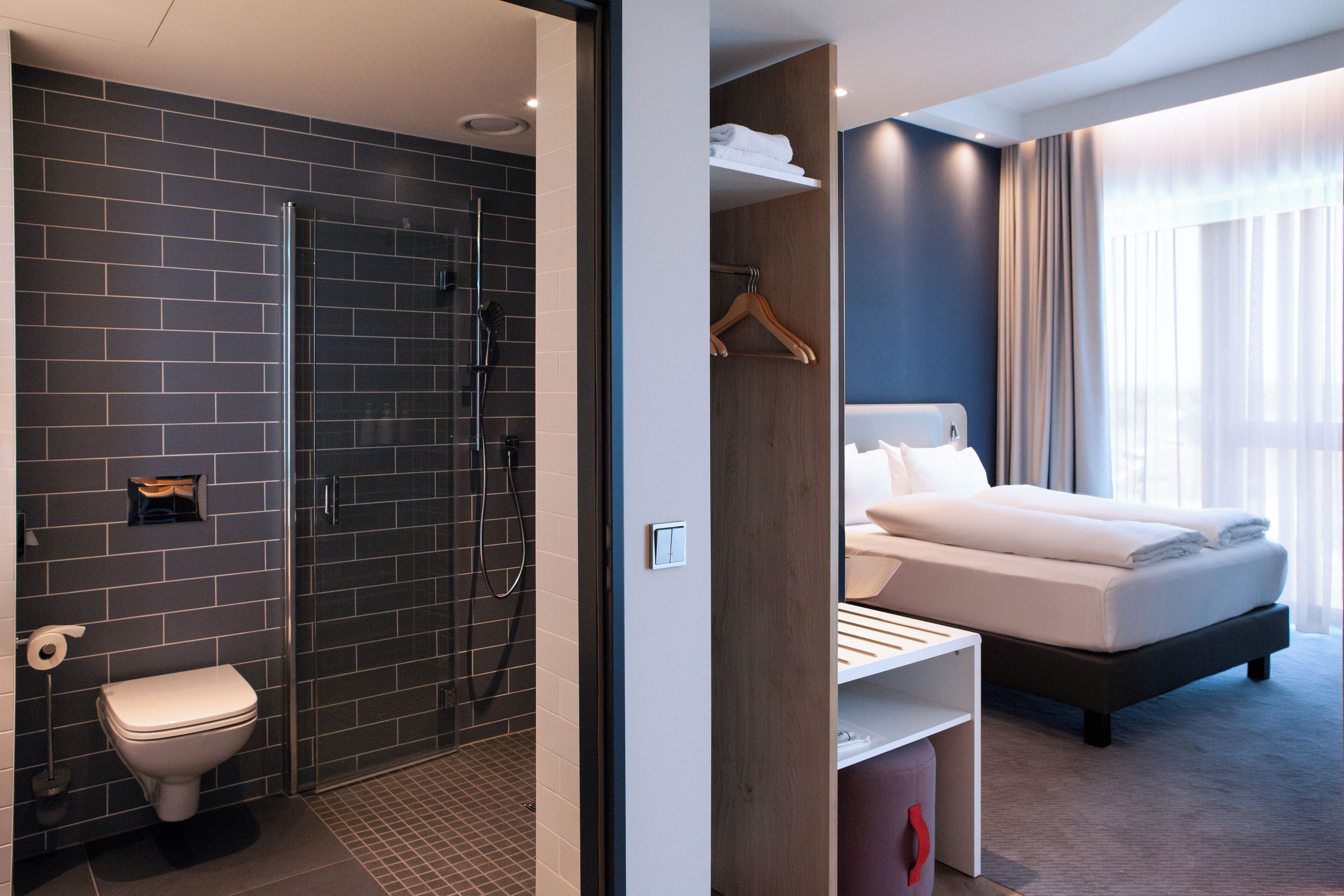 A modern hotel room with a shower, toilet, and a bed with a headboard.
