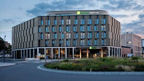 A modern hotel with a curved facade, multiple windows, and a landscaped garden area in front. - Holiday Inn Express & Suites Monheim Am Rhein by IHG (Monheim)