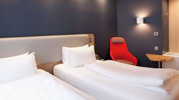 A hotel room with two beds, a red chair, and a small table.