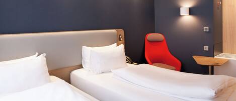 A hotel room with two beds, a red chair, and a small table.