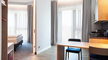 A modern hotel room with a bed, a dining table, and a kitchenette.