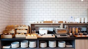 A breakfast buffet setup with various food items, a coffee machine, and stacked plates.
